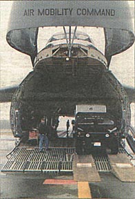 The front end of a cargo aircraft is open. It says "Air Mobility Command."  A vehicle moves down a ramp descending from the cargo hold of the aircraft.