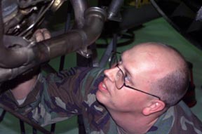 Seen from above, a man in a military uniform looks at metal pipes.