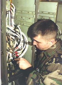A man in a military uniform inspects cabling in a compartment.