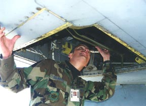 A man in a military uniform looks up into the open hatch on the underside of an aircraft. He has a badge on his uniform.