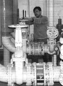 A man stands behind several large pipes and valves.