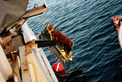 At the side of a ship, a roped pulls wreckage out of the ocean.