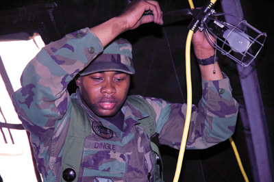 A man in a military uniform attaches an electric light to a cross-beam in a tent.