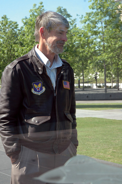 A man in a leather military pilot's jacket stands outdoors.  A patch on his jacket says "U.S. Air Force."