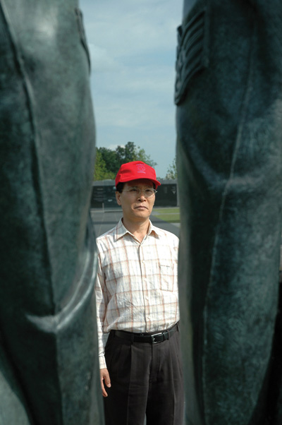 A man in a red hat is framed by two large bronze statues.