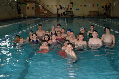 More than 20 children are gathered in a swimming pool together.