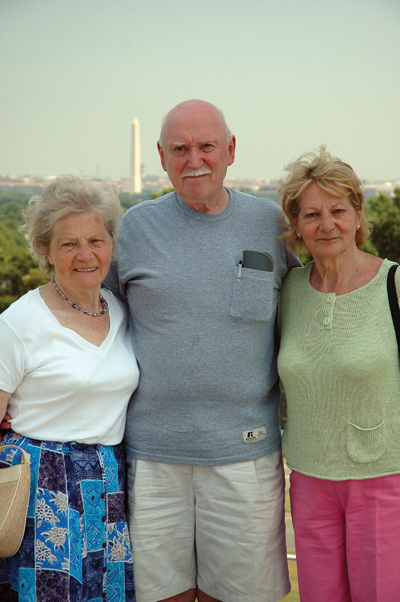 Outdoors, a man is flanked by two women. The Washington Monument is visible behind them.