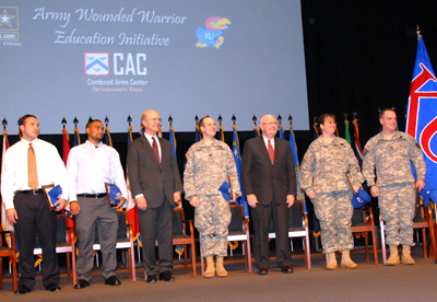 Seven military personnel and civilians stand together on a stage. Behind them a screen says "Army Wounded Warrior Education Initiative."  A row of more than a dozen flags are behind them.  