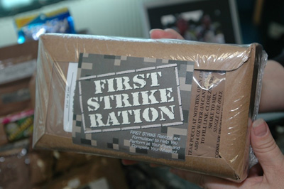 Hands hold a cardboard package wrapped in plastic.  The label says "First Strike Ration."