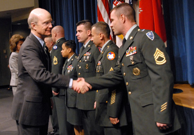 A man in a suit walks down a line of Soldiers and shakes hands with them.