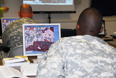 Soldiers sit at computers, which display maps on their screens.