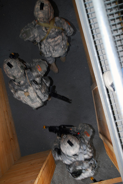 Looking down from above, Soldiers move through a hallway in a mocked-up residential home.