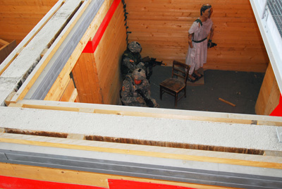 Looking down from above, Soldiers move through one room of a mocked-up residential home.