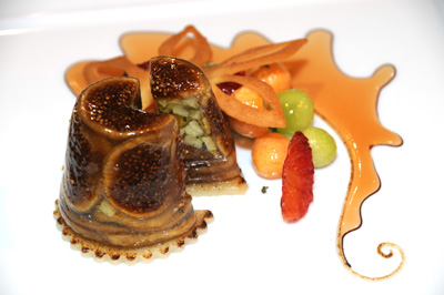 A colorful desert, which includes fruit and a gelled terrine with figs, is displayed on a white plate.