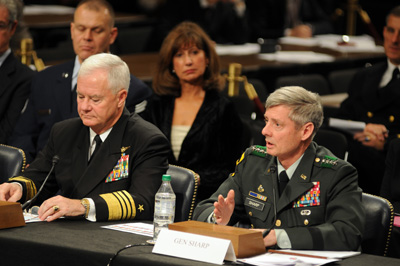 Two men in military uniforms sit at a long table.  One name tag reads "GEN SHARP."  Others sit behind them.