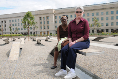 Two women sit on a bench -- one of many.  In the background is the Pentagon.