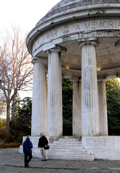 A small rotunda structure stands amidst greenery.  Around the top is says "World War ... A Memorial..."  Two people stand at steps leading up to its platform.