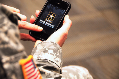 A person in a military uniform holds a cell phone that displays the U.S. Army logo and the words "www.army.mil."