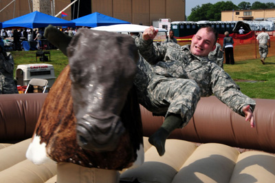 A soldier falls off a mechanical bull into an inflatable air mattress.  
