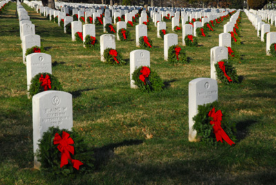 Dozens of identical white headstones are adorned with wreaths made of greenery and red ribbons.