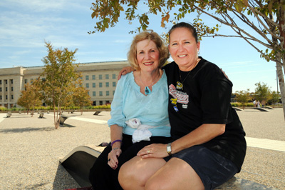 Two ladies sit together on a bench outside.  In the rear is the Pentagon.
