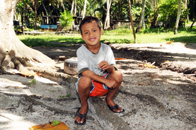 A small boy sits on a root coming out of the base of a tree. 