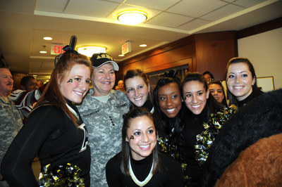 A woman in a military uniform that has four stars on the chest is surrounded by a half-dozen young women in black shirts.  the young ladies have the letter "A" painted on their faces.