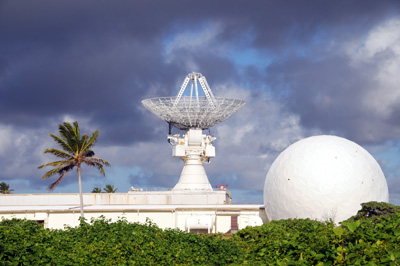 A building with a radar dish on top. To the right is a golf ball-shaped radar dome.  The sky is darkened with grey clouds.