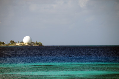 Across a large body of blue and blue-green water are trees and a large golf-ball like radar dome.