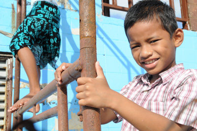 A boy holds onto the bars of scaffolding.  Another child climbs the scaffolding.