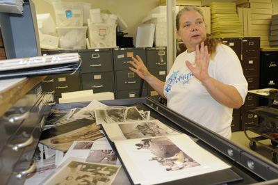 A draw in a flat file is opened, revealing a variety of photos.  A woman stand in front of the drawer.
