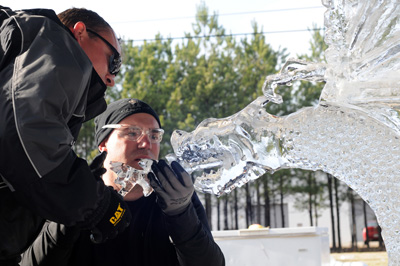 Two men carve a dragon-shaped ice sculpture.