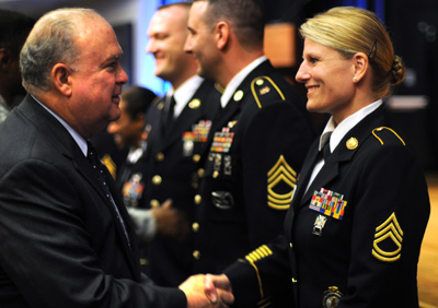 A man in a suit walks down a row of soldiers.  He shakes hands with a female soldier.
