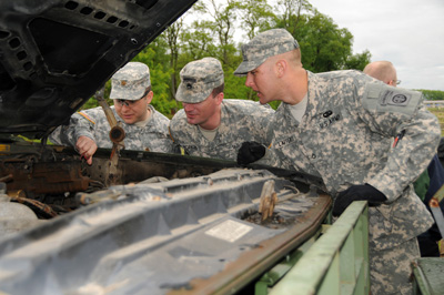 Three soldiers peer into the engine compartment of a vehicle.