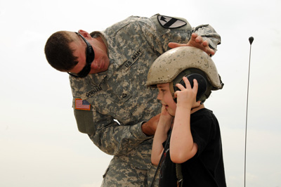 A soldier helps a small boy put on a military helmet.