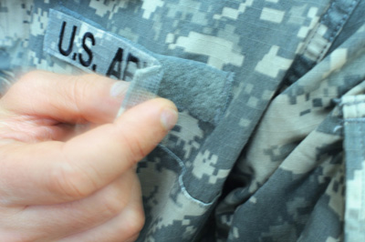 A hand removes the Velcro-backed "U.S. Army" tape from a uniform.
