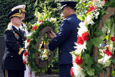 Three men in military uniforms move a wreath.  Other wreaths are nearby.