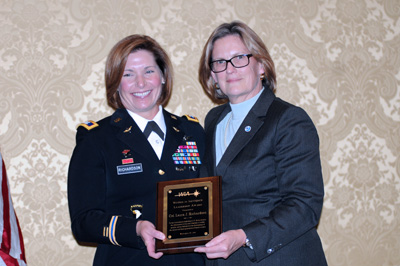 A woman in a military uniform and a woman in a suit hold a plaque.  