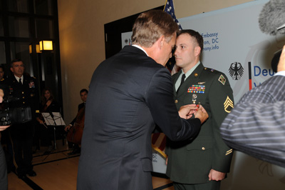 A man in a suit pins a medal on the chest of a man in a military uniform.