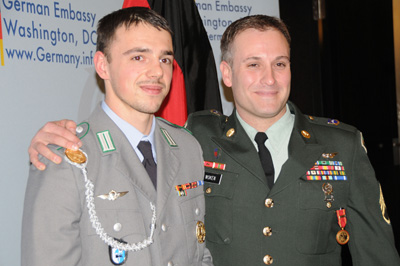 A man in a German military uniform stands next to a man in an American military uniform.