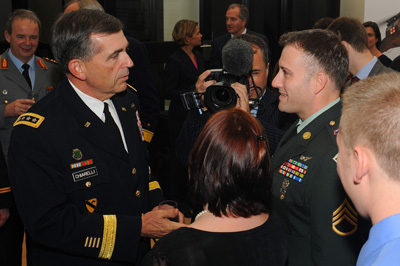 Standing in the middle of a crowd, a military general shakes hand with a sergeant.