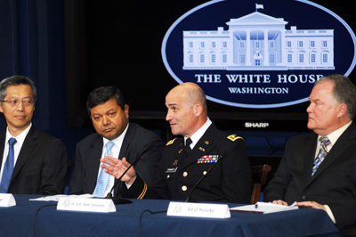 Four men sit at a table.  Behind them is a sign that says "The White House Washington" and an image of the White House.