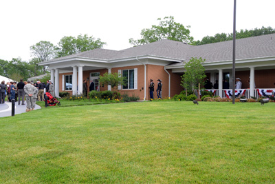 A house with a green lawn.  In front of the house people gather.