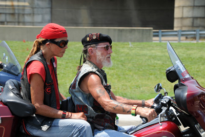 A woman and a man in leather vests ride a motorcycle.