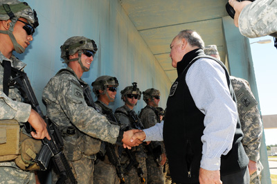 In an outdoor setting, a man in civilian clothes walks down a line of soldiers and shakes their hands.