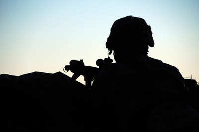 A Soldier with a rifle and a helmet is in silhouette against a blue sky.