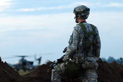 A soldier looks out over a combat scene. In the rear is a helicopter on the ground.  