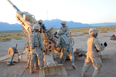 In a desert environment, multiple Soldiers operate a huger howitzer gun.