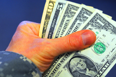 The hand of a uniformed individual holds five U.S. currency bills totaling $18 dollars.