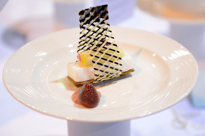 A fancy desert with a lattice of chocolate and a glazed strawberry sits on a small white ceramic plate.